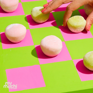 Image of pink and green checkerboard with pink and green My/Mochi balls as pieces and hand reaching to grab a green mochi ball